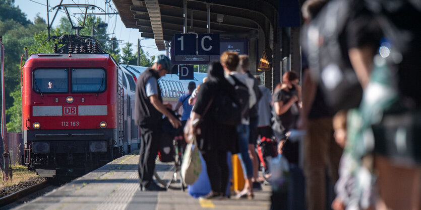 Menschen warten am Bahnsteig, während ein Regionalzug einfährt