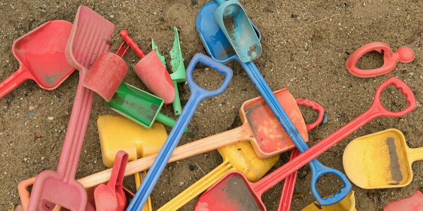 Schaufeln und Eimer liegen auf einem Spielplatz in einem Sandkasten.