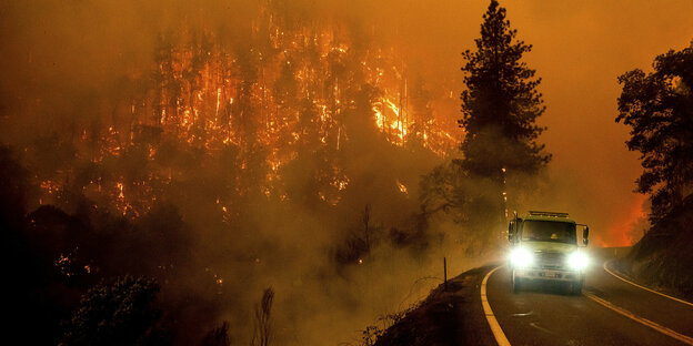 Uma estrada com um veículo, ao fundo uma floresta em chamas.