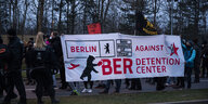 Teilnehmer einer Demonstration gegen den Bau eines geplanten Abschiebezentrums am Flughafen Berlin Brandenburg BER tragen ein Transparent. Darauf steht: "Against BER Detention Center ".