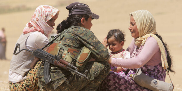 Eine bewaffnete hilft zwei Frauen mit Kind.