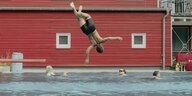 Ein Junge springt vor einem rotes Holzhaus ins Schwimmbecken