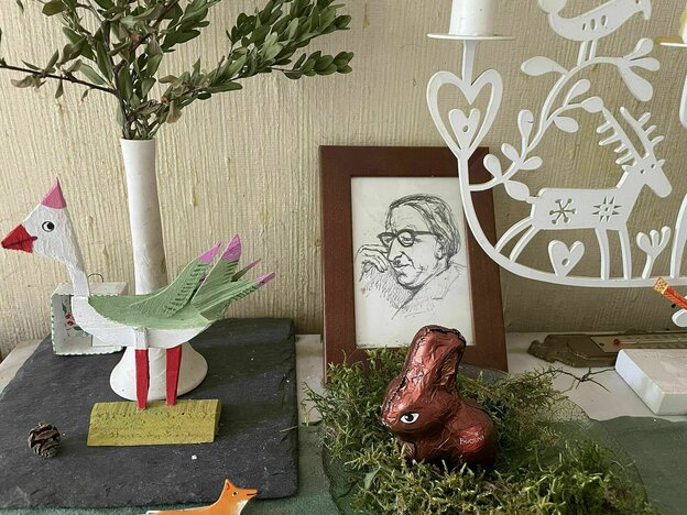 Eine gerahmte Zeichnung mit dem Porträt des Vaters, ein Schokohase in einem Moosbett, ein bemalter Holzvogel und mehr, stehen auf einem Tisch