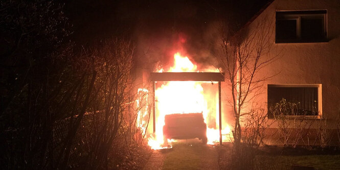 Ein Auto steht direkt neben einem Wohnhaus in Flammen.