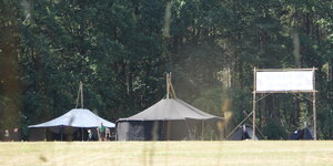 Aus der Ferne sind große, scharze Zelte fotografiert. Daneben Kinder in einheitlicher grün-schwarzer Uniform