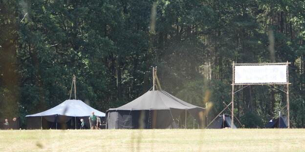 Aus der Ferne sind große, scharze Zelte fotografiert. Daneben Kinder in einheitlicher grün-schwarzer Uniform