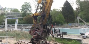 Eine Baggerschaufel vor einem großen, blauem Schwimmbecken