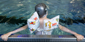 Ein Junge schwimmt in einem Pool, mit Badehaube und Flügel