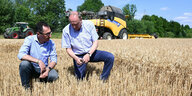 CeCem Özdemir begutachtet mit Joachim Rukwied, dem Präsidenten des Deutschen Bauernverbands, ein Getreidefeid . Im Hintergrund stehen ein Traktor und ein Mähdrescher