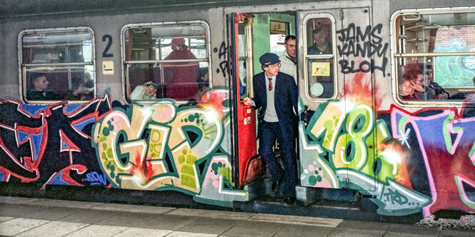 Mit Farben vollgesprühter Zug. Ein Zugbegleiter schaut aus offener Tür.