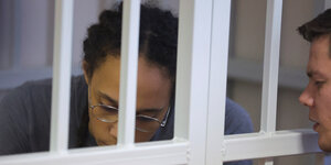 Brittney Griner hinter Gittern bei der Gerichtsverhandlung. Ein Mann nähert sich von rechts den Gitterstäben