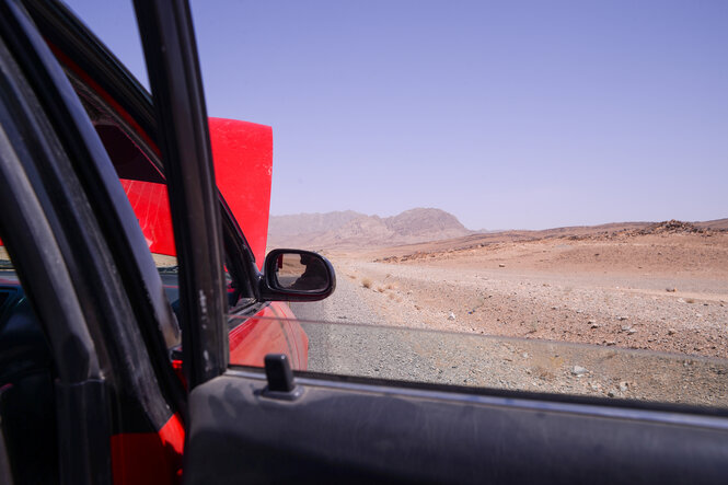 Eine rotes Auto mit geöffneter Motorhaube in karger Landschaft.