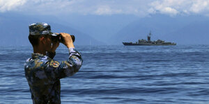 Ein Soldat schaut durch ein Fernglas auf ein Militärschiff im Meer