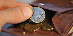 Ein Geldbeutel mit Euromünzen, aus denen jemand eine Ein-Euro-Münze nimmt