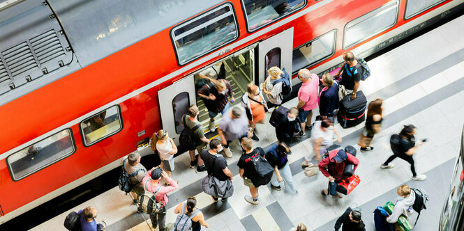 Ein Regionalzug steht am Bahnhof. Das Bild ist von oben aufgenommen worden. Viele Leute sehen vor der Tür, um einzusteigen.