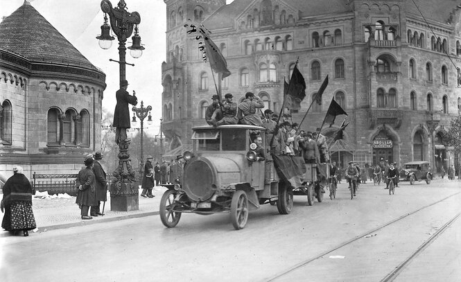 Eine Schwarzweißaufnahme eines Fahrzeugs mit fahnenschwenkenden Personen auf der Ladefläche.