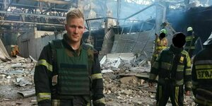 Ein Feuerwehrmann schaut traurig und steht inmitten von Trümmern, im Hintergrund wird aufgeräumt
