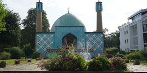 Eine blaugekachelte Moschee mit zwei Minaretten, im Vordergrund Blumenrabatten