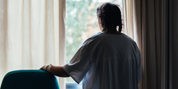 Eine Frau steht im Krankenhauskittel am Fenster