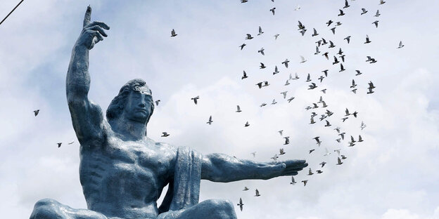 Über der Skulptur eines sitzenden Mannes, der mahnend eine Hand hebt, steigen in Nagasakis Friedenspark Tauben auf.