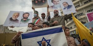 Demonstranten in Teheran vor einer durchlöchteren Israelfahne. Sie zeigen Plakate mit Porträts der Nomenklatura des Gottestaats, General Kasem Soleimani, Mohsen Fakhrizadeh und Ajatollah Khomeini
