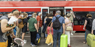 Menschen mit Gepäck auf einem Bahnsteig vor einer Bahn