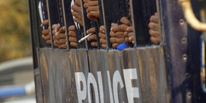 Hände umklammern Gitterstäbe, Aufschrift „Police“
