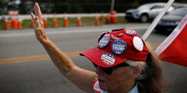 Eine Frau mit rotem Hut, auf dem Trump-Badges angebracht sind, winkt