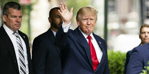 Trump, im Anzug und mit roter Krawatte, winkt