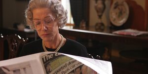 Szene aus dem Film "The Queen": Die Queen, gespielt von Helen Mirren, sitz an einem Tisch und liest eine Zeitung, sie trägt eine Brille