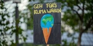 Ein Plakat wird hochgehalten, es zeigt eine Eistüte, statt einer Eiskugel liegt eine schmelzende Welt obenauf. Beschriftet: "Geh wählen fürs Klima"