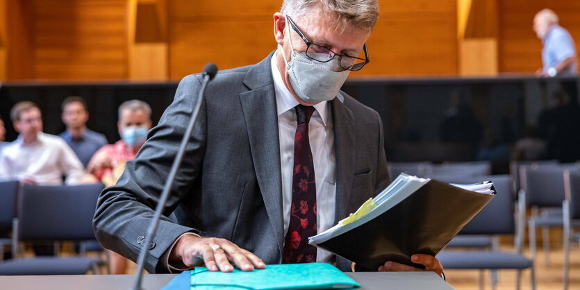 Ein Mann mit Corona-Maske blättert in einem Aktenordner