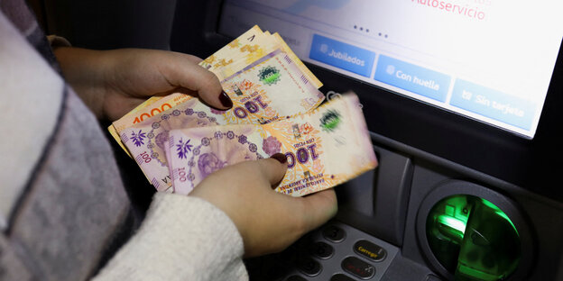 Eine Person zählt Geldscheine an einem Geldautomaten.
