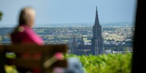 Eine Frau sitzt an einem Aussichtspunkt auf das Ulmer Münster in der Sonne