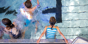 Ein Junge und zwei Mädchen schwimmen in einem Hallenbad-Becken