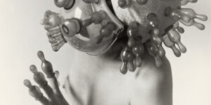 Auf einem Ausschnitt eines Fotos tanzt eine unbekleidete Frau, über ihre Finger hat sie Saugaufsätze für Babytrinkflaschen gezogen, auch ihre Maske hat solche Aufsätze