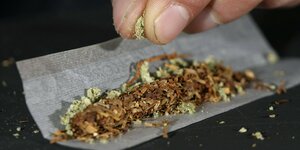 Finger zerbröseln Marihuana in einen Joint.