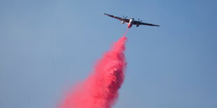 Ein Flugzeug verteilt rotes Löschmittel.