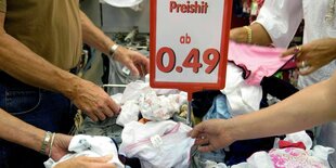 Hande wühlen an einem Grabbeltisch in Unterwäsche. Preisschild verkündet 0,49 Cent