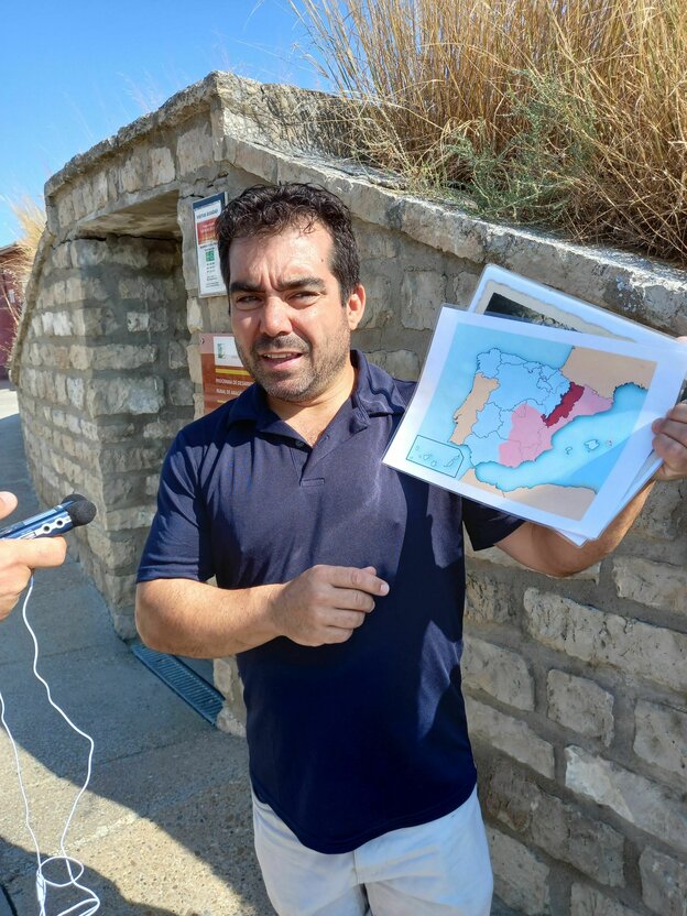 Der Bürgermeister steht im Freien vor einer Mauer und hält eine Landkarte in die Höhe