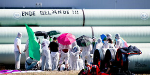 Aktivisten stehen vor gelagerten Rohrleitungen auf der Baustelle für die geplante Gaspipeline am Jade-Weser-Port und haben darauf die Aufschrift ·Ende Gelände· geklebt.