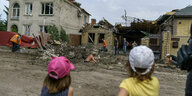Kinder stehen vor einem zerstörten Haus, das von Menschen wieder aufgebaut wird