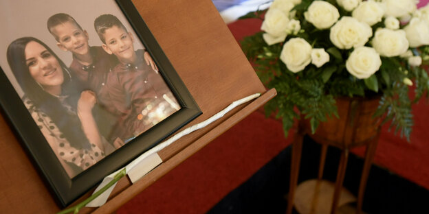 Auf einem Tisch steht ein Foto mit Trauerflor, auf dem Bild sind eine Frau und ihre beiden Kinder zu sehen.