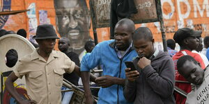 Drei Männer in Nairobi stehen auf der Straße und schauen interessiert auf ihre Smartphones