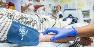 Eine Pfleger:in hält den Arm eines Patienten in einer Notaufnahme