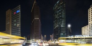 Das Foto zeigt einen wenig erleuchteten Potsdamer Platz in Berlin mit hell erleuchteten Straßenverkehr im Vordergrund.