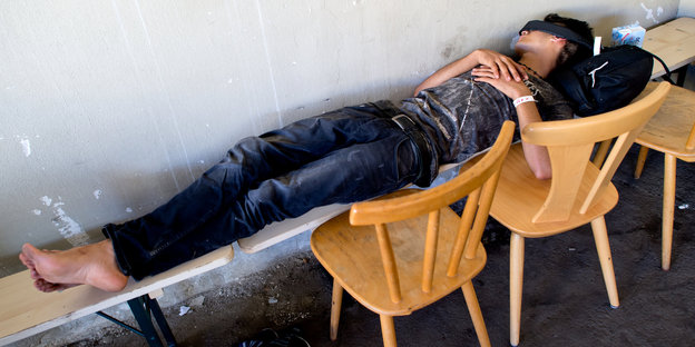 Mensch liegt bei Tageslicht schlafend auf einer Bierbank
