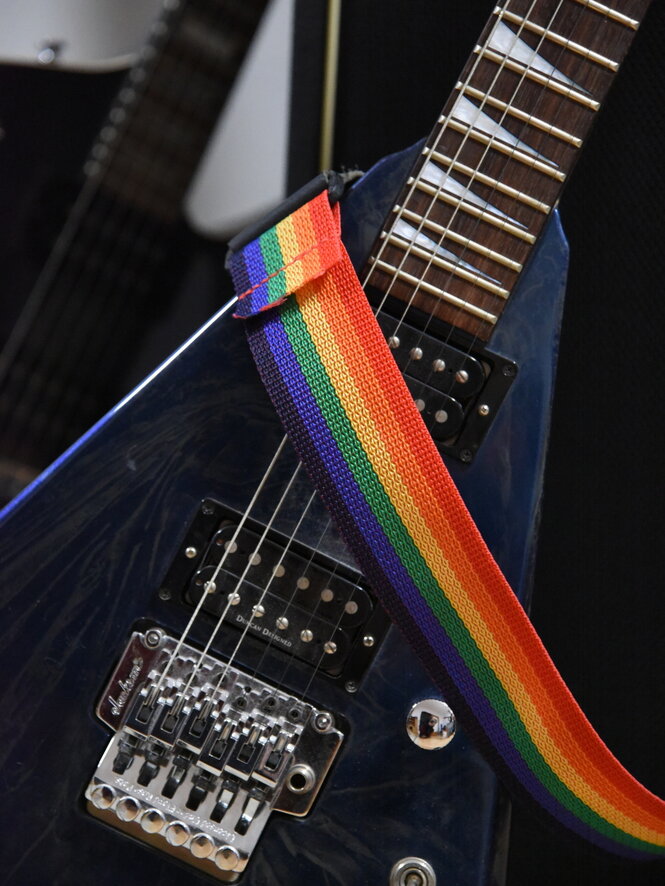 Ein Haltegurt in Regenbogenfarben über Gitarrensaiten