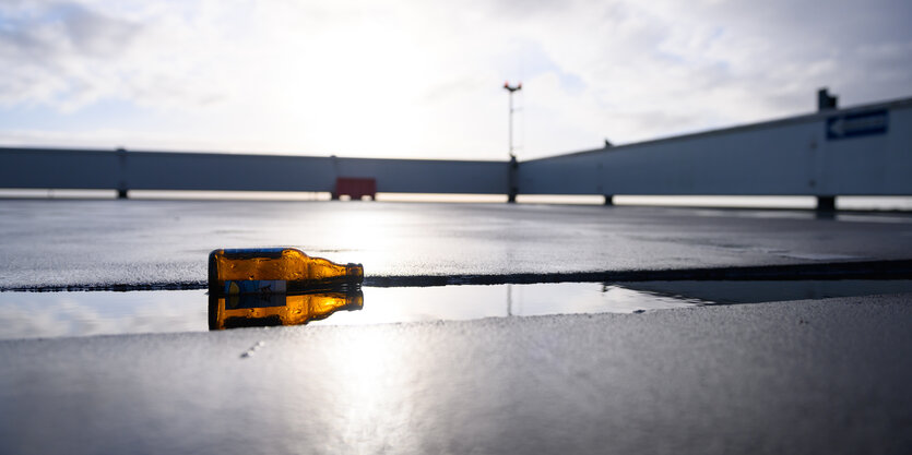 Eine leere Bierflasche liegt auf der Seite auf einem leeren Parkdeck in einer Pfütze