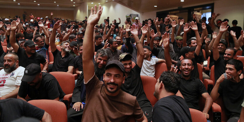 Menschen in einem Saal lachen und heben die Hände